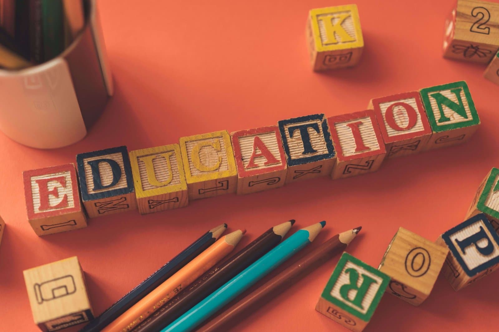 Wooden alphabet blocks spelling EDUCATION beside coloured pencils
