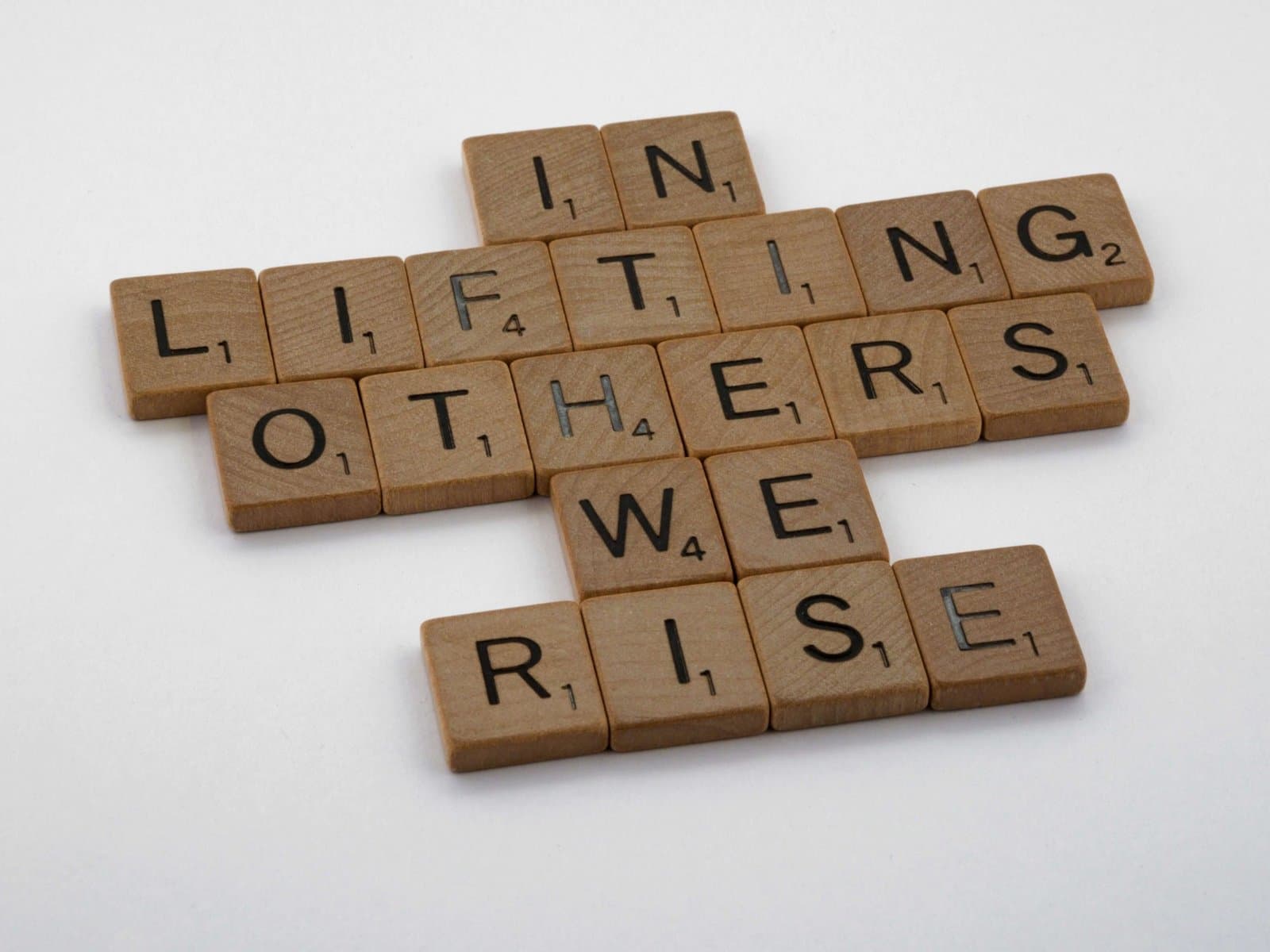 Letter tiles spelling “In lifting others we rise”