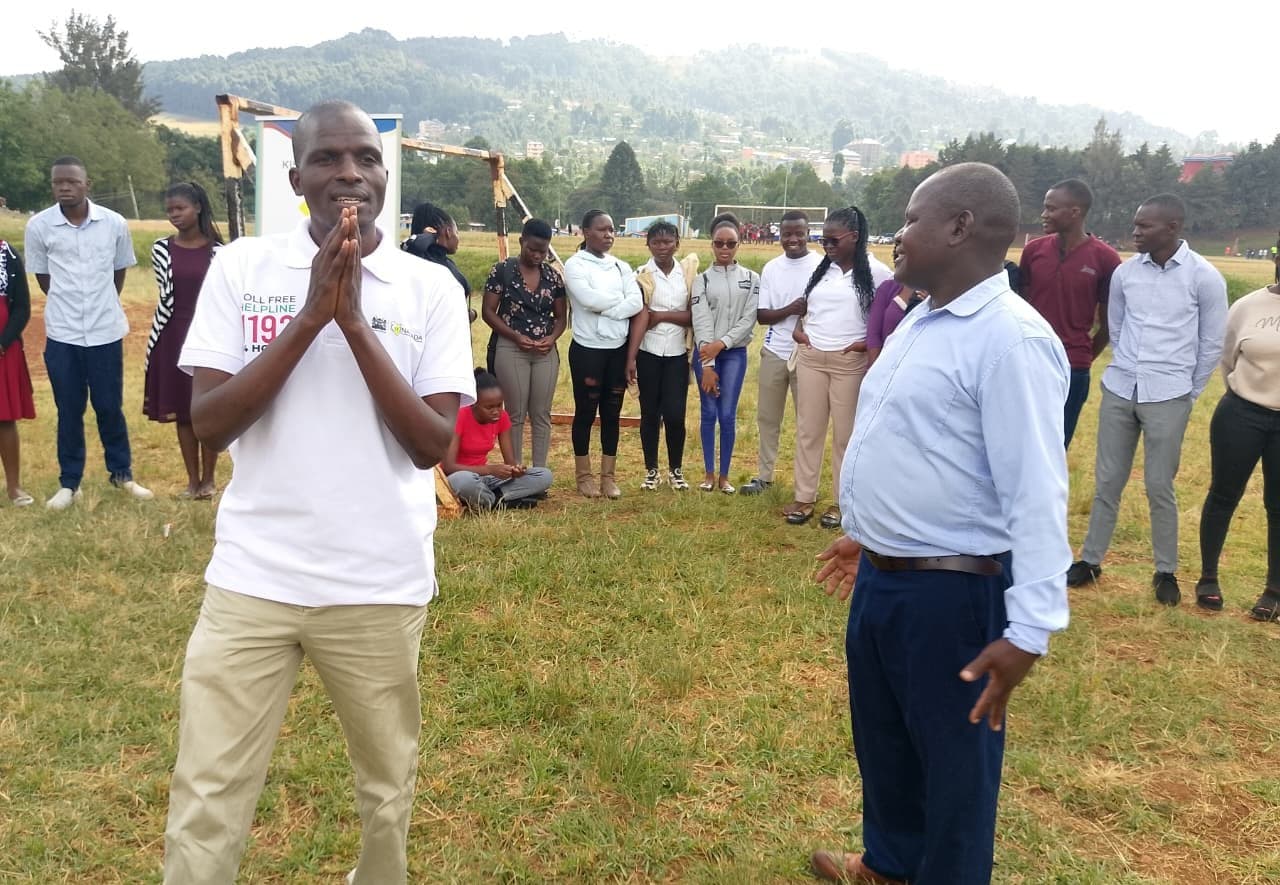 A YoNISeRD facilitator addressing young people and community leaders gathered on a field