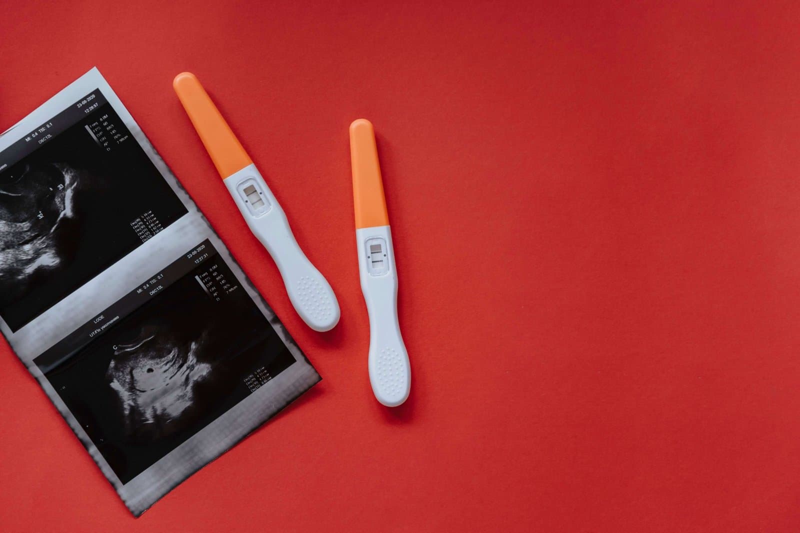 Two pregnancy tests and an ultrasound print on a red background