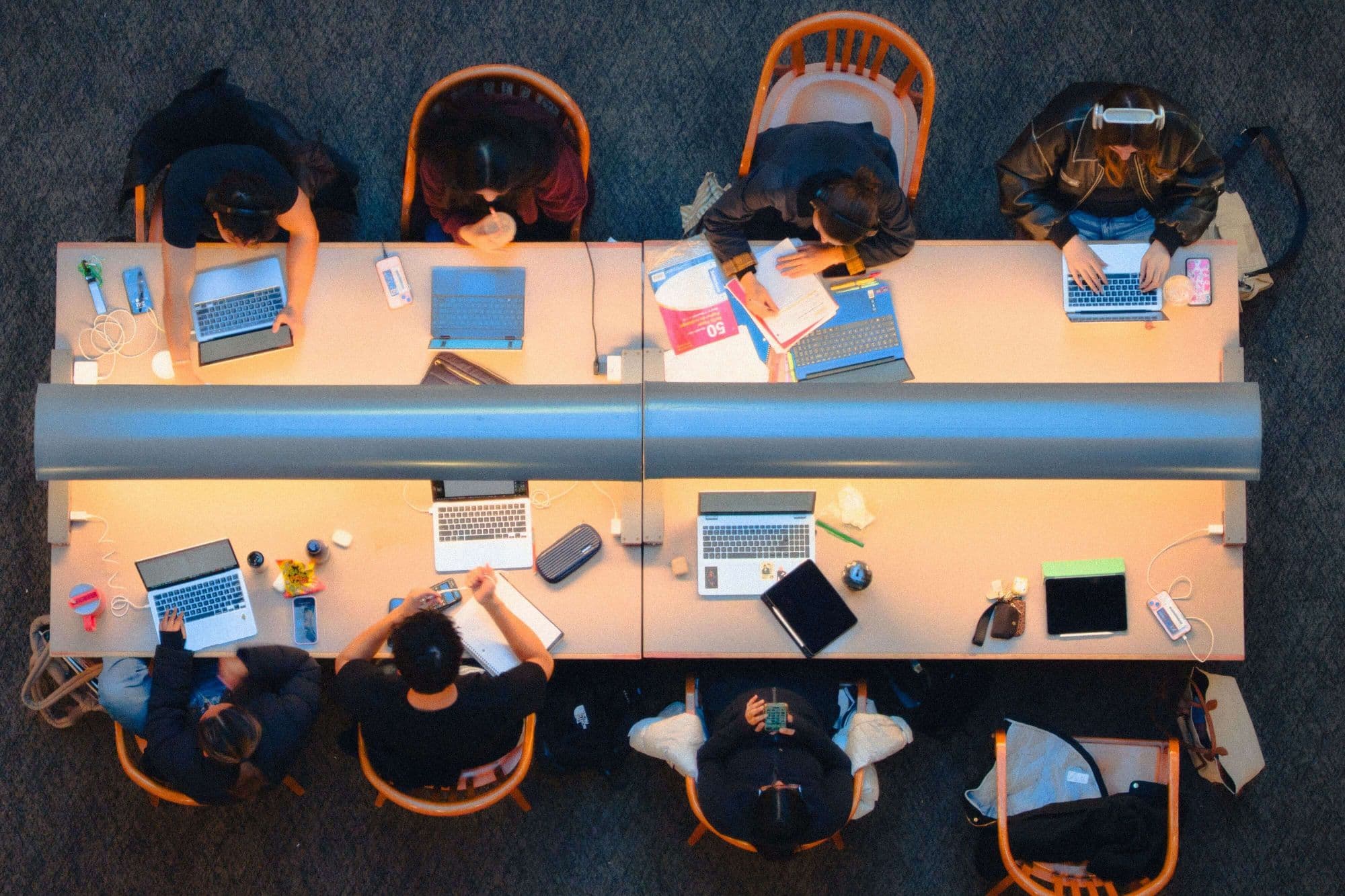 Young people working together on laptops and notes around shared study tables